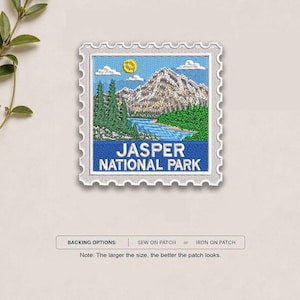 May include: A square embroidered patch shaped like a postage stamp featuring a mountain landscape with a blue lake, green pine trees, and a yellow sun in a blue sky. The text JASPER NATIONAL PARK is printed in white on a blue background at the bottom.