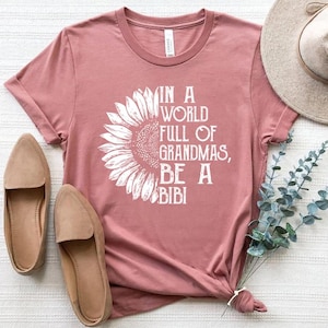 May include: A pink t-shirt with a white sunflower graphic and the text "In a world full of grandmas, be a bibi".