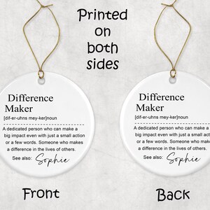May include: Two-sided white ceramic ornament with gold string. The ornament features the definition of "Difference Maker" in black text. The front and back of the ornament are visible, with the word "Front" and "Back" at the bottom.