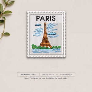 May include: A rectangular embroidered patch with a scalloped edge featuring a brown Eiffel Tower, green trees, and blue clouds against a white background. The word PARIS is stitched in black at the top. Text below reads BACKING OPTIONS: SEW ON PATCH or IRON ON PATCH.