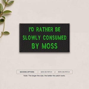 May include: A rectangular black embroidered patch featuring the bright green text "I'D RATHER BE SLOWLY CONSUMED BY MOSS". Below the patch, a label displays "BACKING OPTIONS: SEW ON PATCH or IRON ON PATCH" and a note about patch sizing.