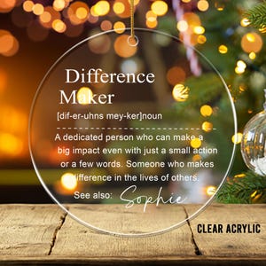 May include: Clear acrylic ornament with the text "Difference Maker" and a definition. The ornament has a gold string for hanging and the name "Sophie" is written below the definition. The words "CLEAR ACRYLIC" are at the bottom.