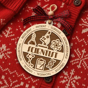 May include: A wooden Scientist ornament with a brown center and light wood outer ring. The ornament features science-related icons and the word "SCIENTIST". It hangs from a twine loop and a red and black plaid ribbon. The ornament is set against a red sweater.