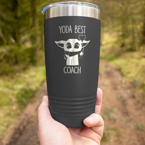 K&ouml;nnte beinhalten: Ein dunkelgrauer Edelstahlbecher mit einer wei&szlig;en Grafik eines Comic-Charakters, der einen herzf&ouml;rmigen Ballon h&auml;lt. Der Text "Yoda Best Coach" ist auf den Becher gedruckt.