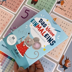Könnte beinhalten: Ein blaues und weißes Lernspielkartenset für Kinder mit einer Comicmaus, die einen Bleistift hält. Das Kartenset ist mit "Das kleine EINMALEINS" betitelt und enthält 30 Karten mit Multiplikationsaufgaben.