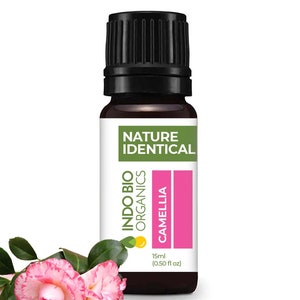 May include: A brown glass bottle of Indo Bio Organics Camellia essential oil. The label features the text "NATURE IDENTICAL" and "INDO BIO ORGANICS". The bottle is 15ml (0.50 fl oz). Pink and white camellia flowers are in the foreground.