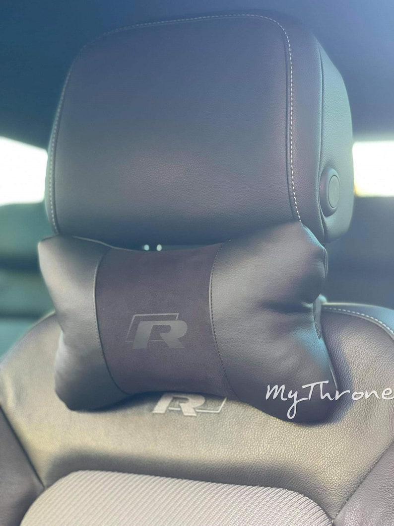 May include: Black leather car seat with a black headrest and a black pillow with an embroidered "R" logo. The pillow is positioned on top of the headrest. The text "my Throne" is visible in the lower right corner of the image.