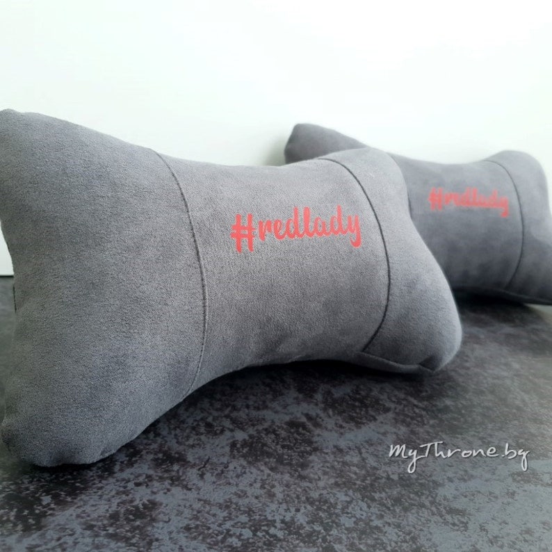 May include: Two gray car neck pillows with the text "#redlady" embroidered in red on one pillow.