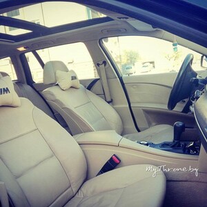 May include: Beige leather interior of a car with a sunroof. The front seats have headrests with the BMW logo.