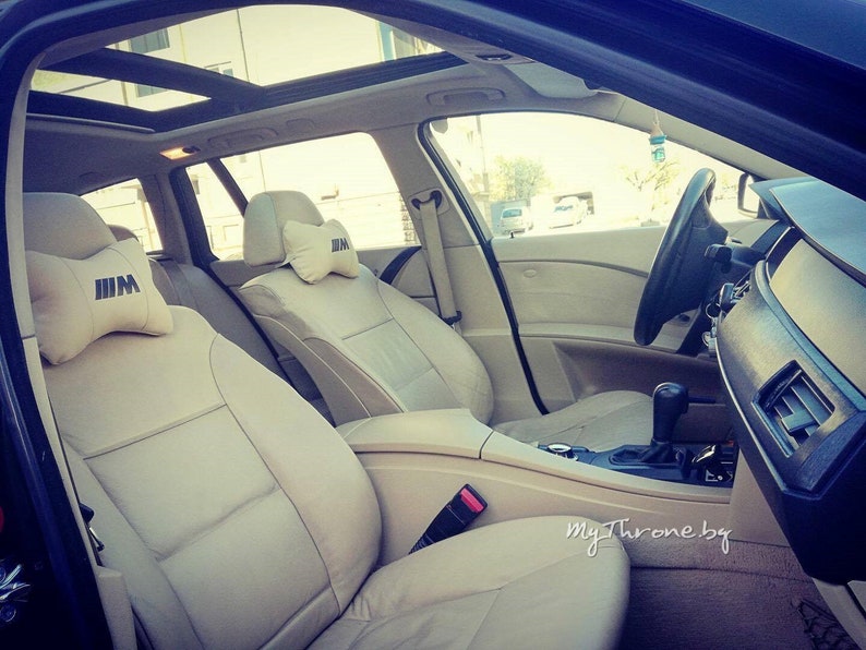 May include: Beige leather interior of a car with a sunroof. The front seats have headrests with the BMW logo.