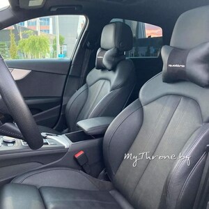 May include: Black leather car interior with two front seats. The driver's seat has a black steering wheel and a black dashboard. The passenger seat has a black headrest with the word "quattro" printed on it.