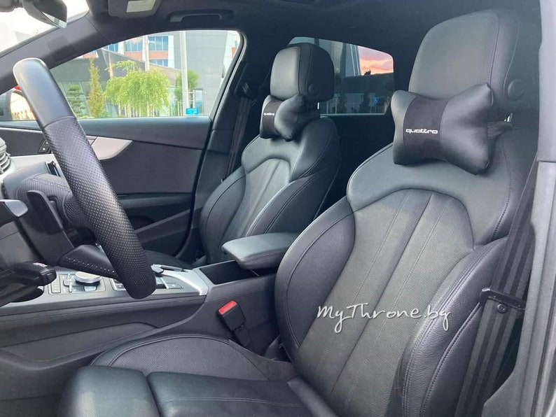 May include: Black leather car interior with two front seats. The driver's seat has a black steering wheel and a black dashboard. The passenger seat has a black headrest with the word "quattro" printed on it.