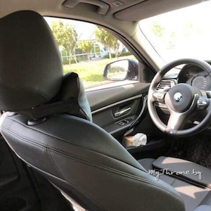 May include: Black leather car seat with a headrest and a steering wheel. The steering wheel has a silver BMW logo.