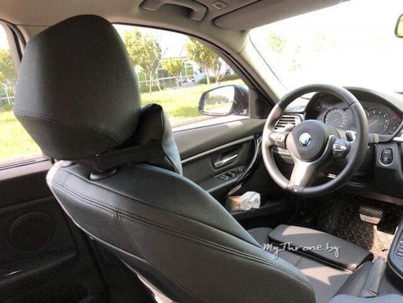 May include: Black leather car seat with a headrest and a steering wheel. The steering wheel has a silver BMW logo.