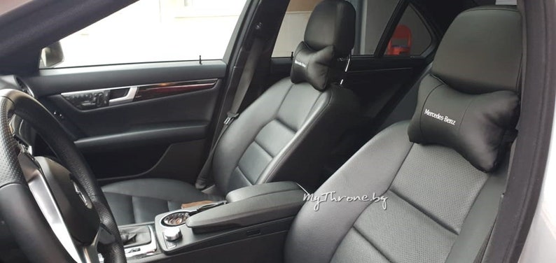 May include: Black leather car seats with a black headrest pillow that says "Mercedes Benz" on it.
