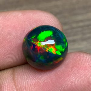 May include: A round black opal gemstone with green, red, and orange flashes of color.
