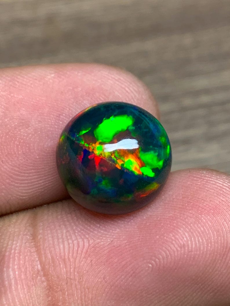 May include: A round black opal gemstone with green, red, and orange flashes of color.