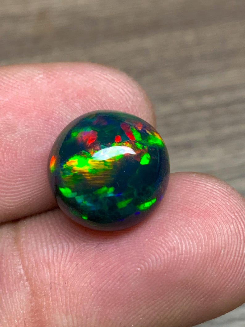 May include: A round, black opal gemstone with green, red, and orange flashes of color.