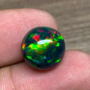 May include: A round black opal gemstone with green, red, and blue iridescent flashes.