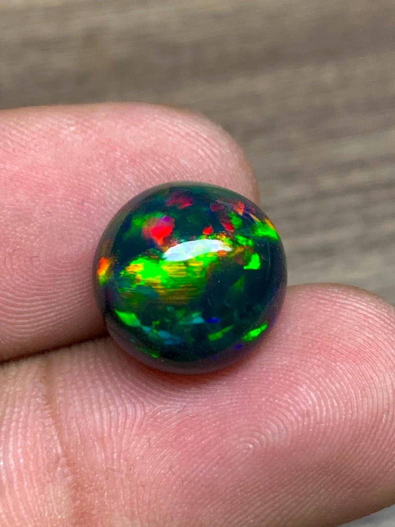 May include: A round black opal gemstone with green, red, and blue iridescent flashes.
