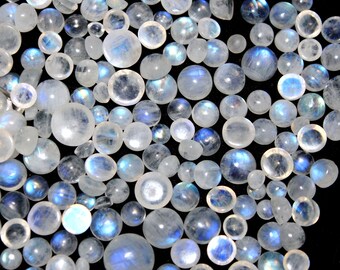 Puede incluir: Una colección de cabujones de piedra lunar iridiscente en varios tamaños. Las piedras son de color blanco lechoso con un brillo azul.