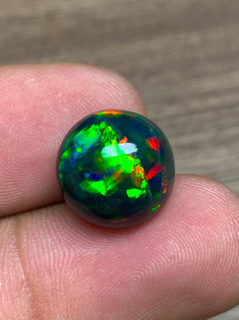 May include: A round black opal gemstone with green, red, and orange flashes of color.