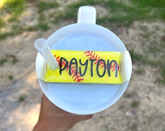 May include: A white tumbler with a yellow and red softball-themed lid. The lid has the name "PAYTON" written in black lettering.