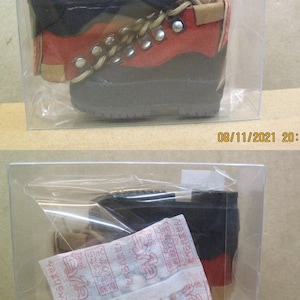 May include: A pair of red and black hiking boots with brown laces and metal eyelets. The boots are in a clear plastic container with a white label that says "MDD".