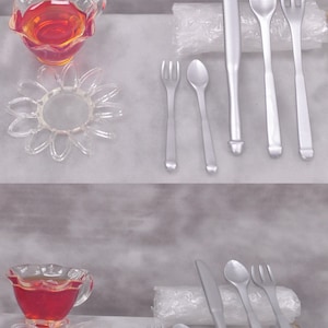 May include: A set of silver-coloured miniature cutlery, including a knife, fork, and spoon, arranged on a white surface. The cutlery is displayed next to a clear plastic bag and a small, clear glass teacup filled with red liquid.