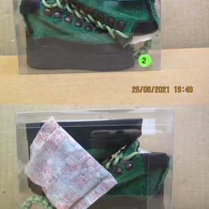 May include: A pair of green suede boots with black laces and a black sole. The boots are in a clear plastic box with a white label that says "限定色" and "OUTLET".