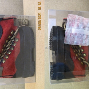 May include: Two pairs of red and black hiking boots with gold accents and laces. The boots are displayed in clear plastic boxes. One box has a small white packet with text in Japanese.