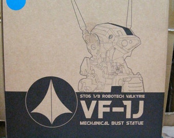 May include: A cardboard box with a black and white illustration of a robot head. The box is labeled "ST06 1/8 ROBOTECH VALKYRIE VF-1J MECHANICAL BUST STATUE" and "ROBOTECH".