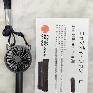 May include: A black handheld fan with a cat-shaped design. The fan is attached to a black lanyard. The packaging includes the text "ニャンディ・ファン L 1/3 (60cm) ドール用" which translates to "Nyandy Fan L 1/3 (60cm) Doll Use".