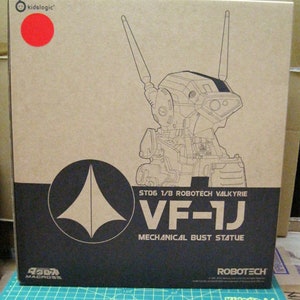 May include: A cardboard box with a line drawing of a robot on the front. The box is brown with black text that reads "ST06 1/8 ROBOTECH VALKYRIE VF-1J MECHANICAL BUST STATUE ROBOTECH".