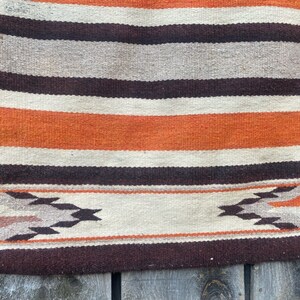 May include: A woven rug with a striped pattern in shades of brown, orange, and white. The rug has a geometric design at the bottom.