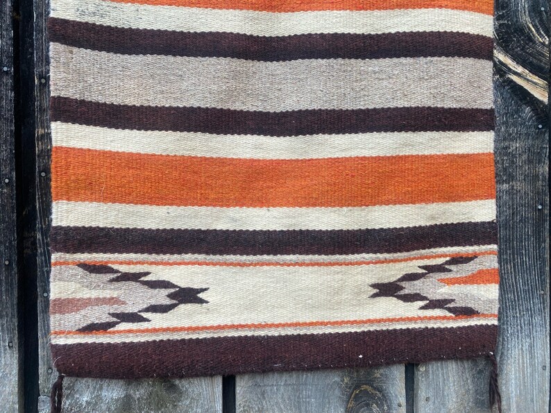 May include: A woven rug with a striped pattern in shades of brown, orange, and white. The rug has a geometric design at the bottom.