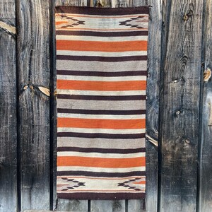 May include: A woven rug with a striped pattern in shades of brown, orange, and white. The rug has a geometric design at the top and bottom.