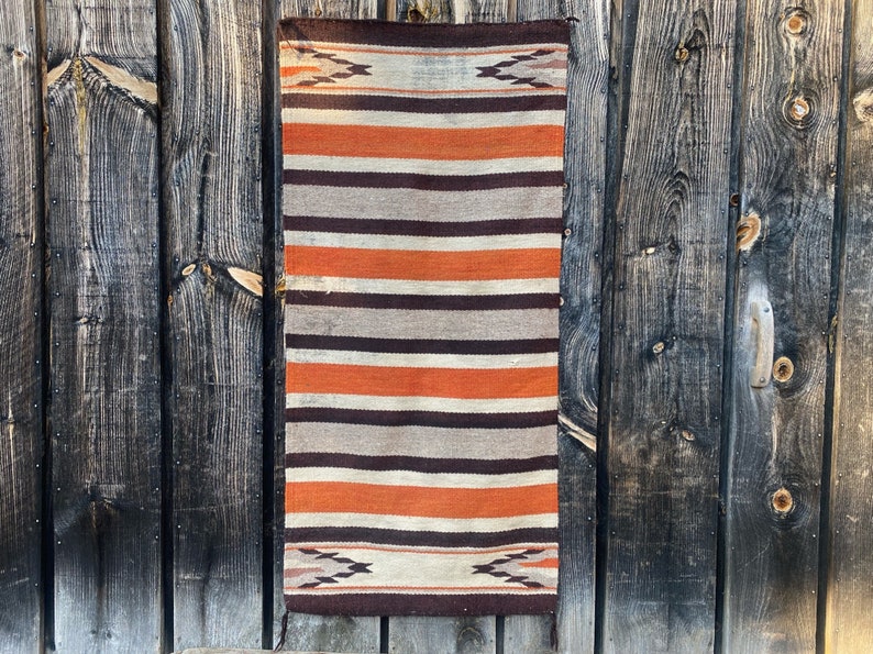 May include: A woven rug with a striped pattern in shades of brown, orange, and white. The rug has a geometric design at the top and bottom.