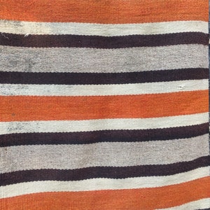 May include: A striped woven rug with orange, white, and brown stripes. The rug is hanging on a dark wood wall.
