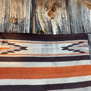 May include: A woven rug with a brown, white, and orange striped pattern. The rug has a geometric design in the top band.