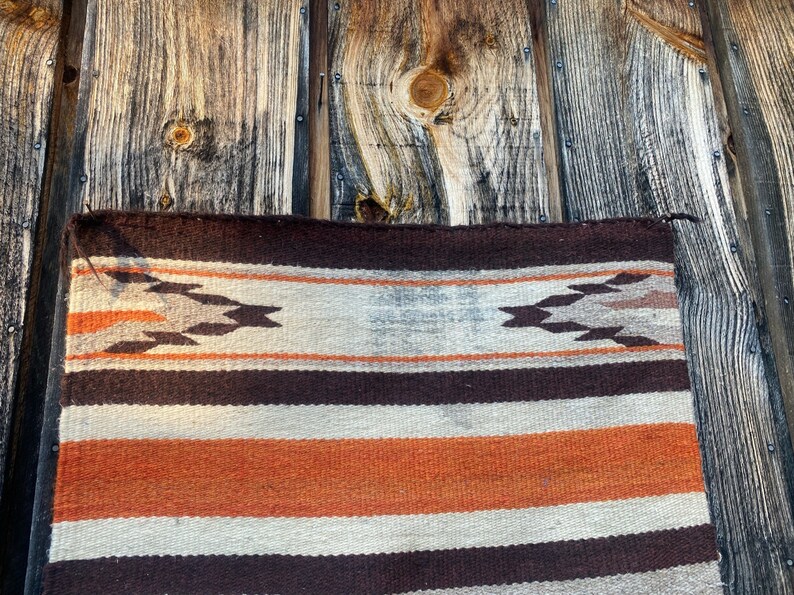 May include: A woven rug with a brown, white, and orange striped pattern. The rug has a geometric design in the top band.