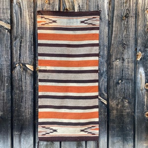 May include: A woven rug with a striped pattern in shades of brown, orange, and white. The rug has a geometric design at the top and bottom.