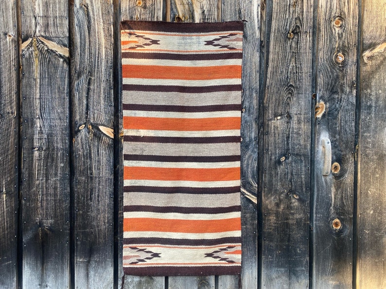 May include: A woven rug with a striped pattern in shades of brown, orange, and white. The rug has a geometric design at the top and bottom.