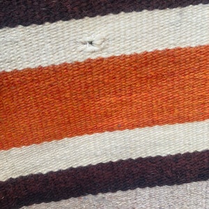 May include: A woven rug with horizontal stripes in brown, white, and orange. The rug has a small hole in the center.