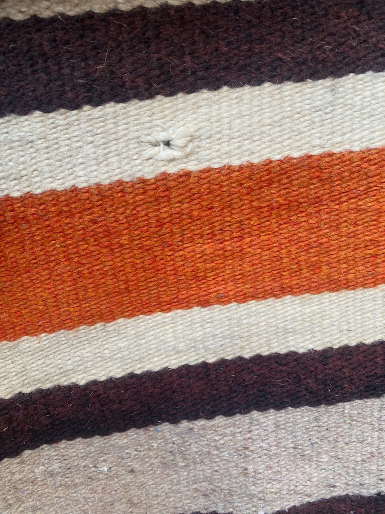 May include: A woven rug with horizontal stripes in brown, white, and orange. The rug has a small hole in the center.