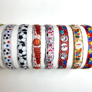 May include: Assortment of colorful ribbon with various designs, including sports, school, and children's themes. The ribbons are white with colorful designs, including baseball, soccer, basketball, cheer, Thing 1 and Thing 2, back to school, and a puzzle pattern.