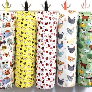 May include: Five fabric bag dispensers hanging on hooks. The dispensers are made of white fabric with different colorful patterns. One has a yellow background with black and white chickens, another has a white background with red and black ladybugs, another has a white background with colorful chickens, another has a white background with a black and white chicken, and the last one has a green background with brown horses and white sheep.