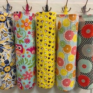 May include: Five fabric bags with different patterns hanging on hooks. The bags are made of a white fabric with various colorful patterns, including floral, owls, chickens, citrus fruits, and large flowers.