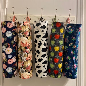 May include: Five different patterned kitchen aprons hanging on hooks. The aprons are in various floral, animal print, and alphabet designs.