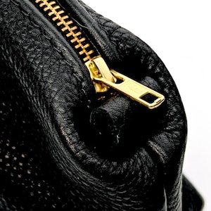 May include: Close-up of a black leather zippered pouch with a gold zipper.